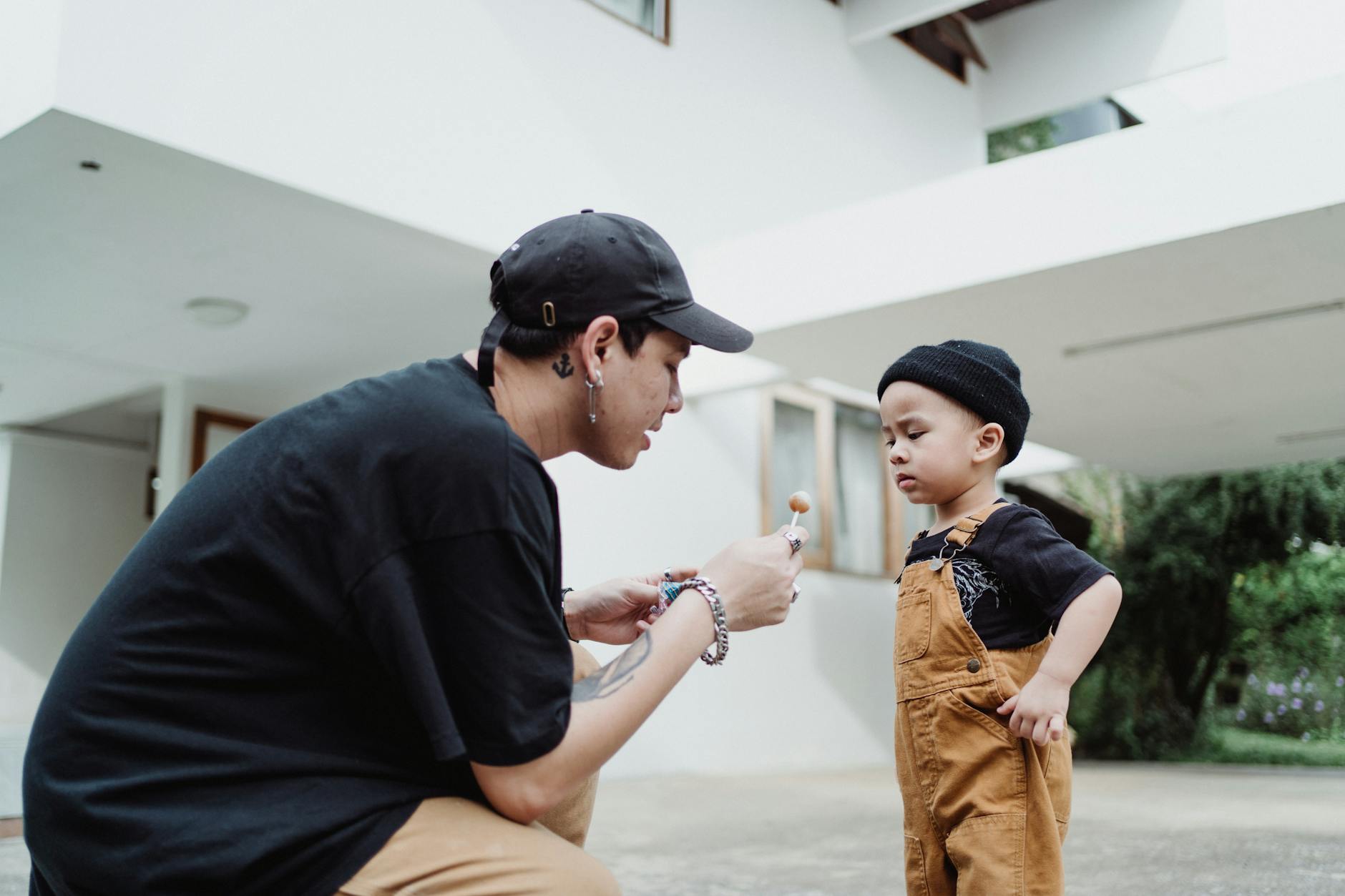 man giving a lollipop to a baby boy in front of a house
