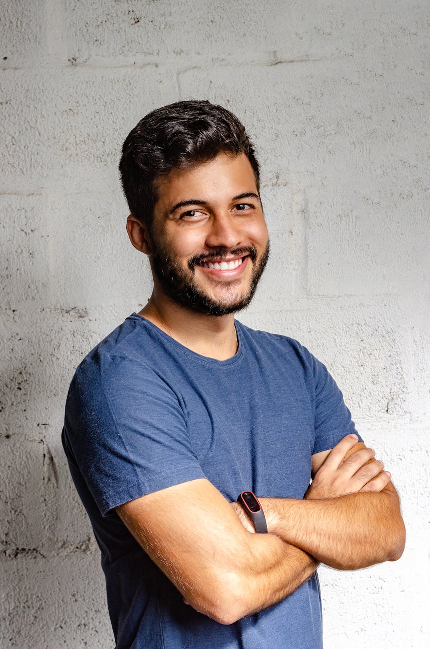 portrait photo of smiling man with his arms crossed standing in front of a wall